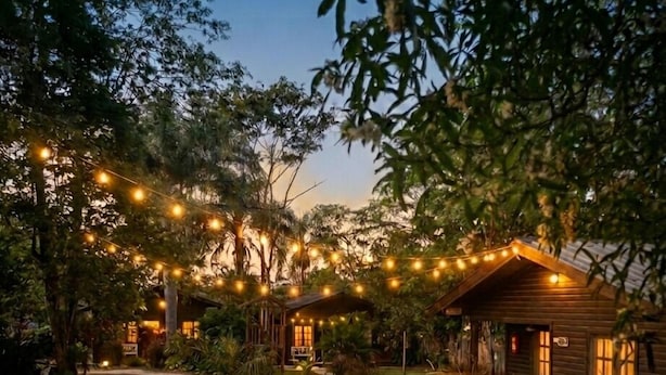 A rustic cabin with a porch, surrounded by a well-maintained lawn and string lights.
