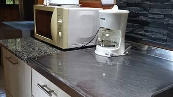 A kitchen with a microwave, coffee maker, granite countertop, and a brick wall.