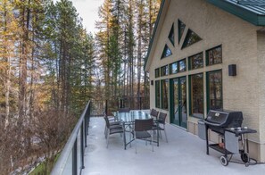 A covered outdoor area with a barbecue grill, seating, and a view of a forest. - Lakefront Tie Lake l Hot Tub l Pool Table l A/C (Jaffray)