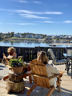 Two people seated on wooden chairs facing a waterfront view with a dock and boats. - Lux. Waterfront Cottage, Amazing Water Views /Fire Pit /Central/5km-MTB & Beach (George Town)