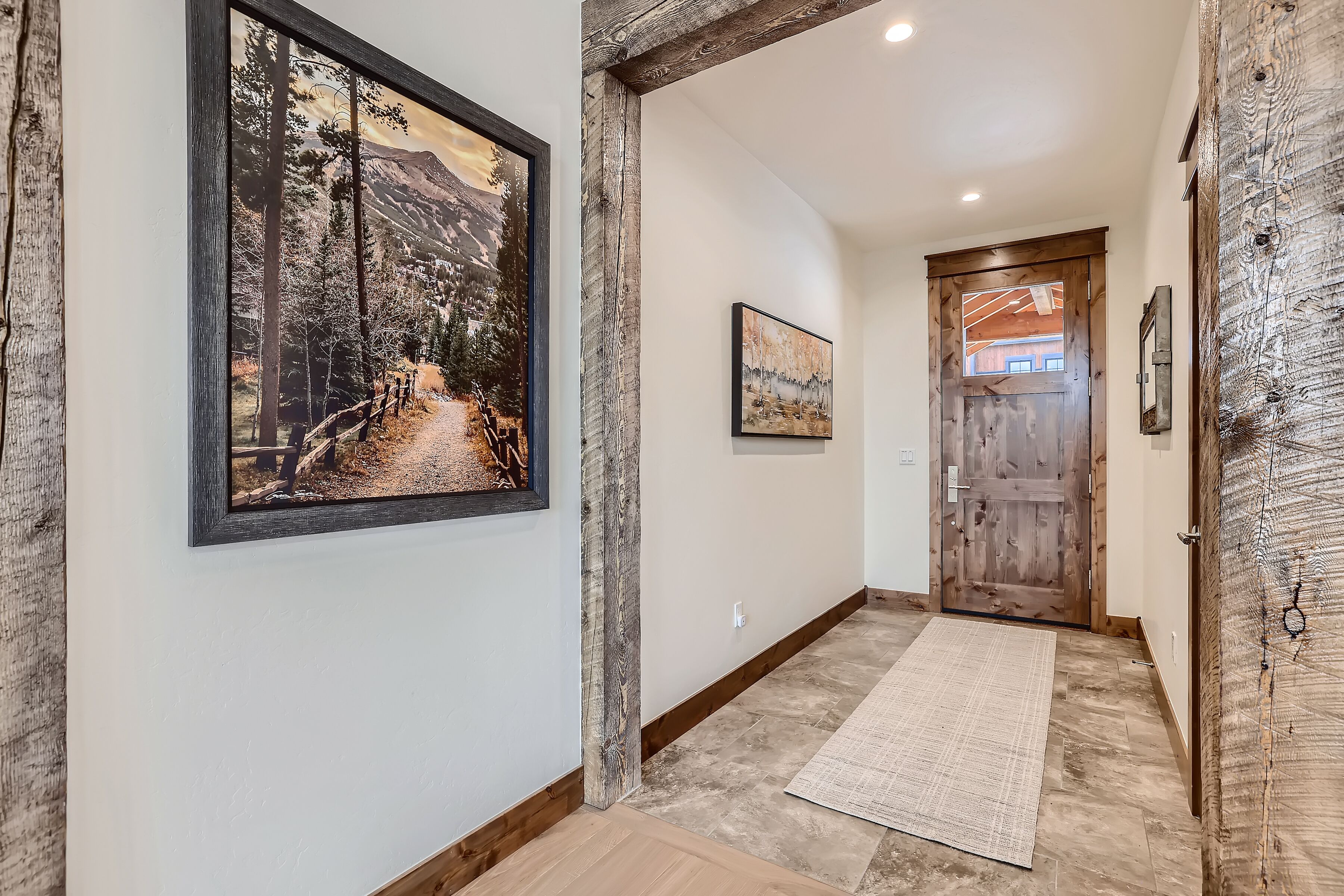 A hallway with rustic wooden beams, a framed landscape painting, a wooden door, and a textured rug.