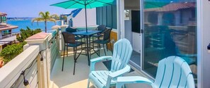 Un balcon avec une table et des chaises, donnant sur une étendue d’eau et des palmiers.