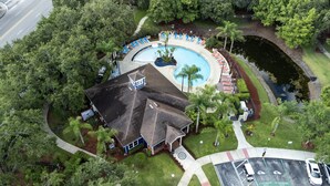 Vue aérienne d’un complexe hôtelier doté d’une piscine, de chaises longues et d’un espace couvert avec un toit.