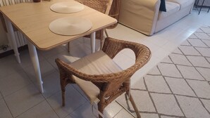 Olohuoneessa on puinen ruokapöytä, punottu rottinkituoli, beige sohva ja ruukussa oleva viherkasvi.