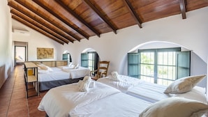 Une chambre d’hôtel avec trois lits, un plafond en bois et de grandes fenêtres.