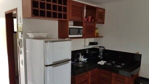 A compact kitchen with a white refrigerator, a microwave, a stove, and wooden cabinets. - Flat no Condomínio Brisas do Amor (RN)
