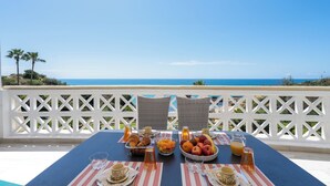 A table set for breakfast with a view of the ocean, white lattice railing, and wicker chairs. - Oceanfront adorable one bedroom apart in Albufeira (Albufeira)