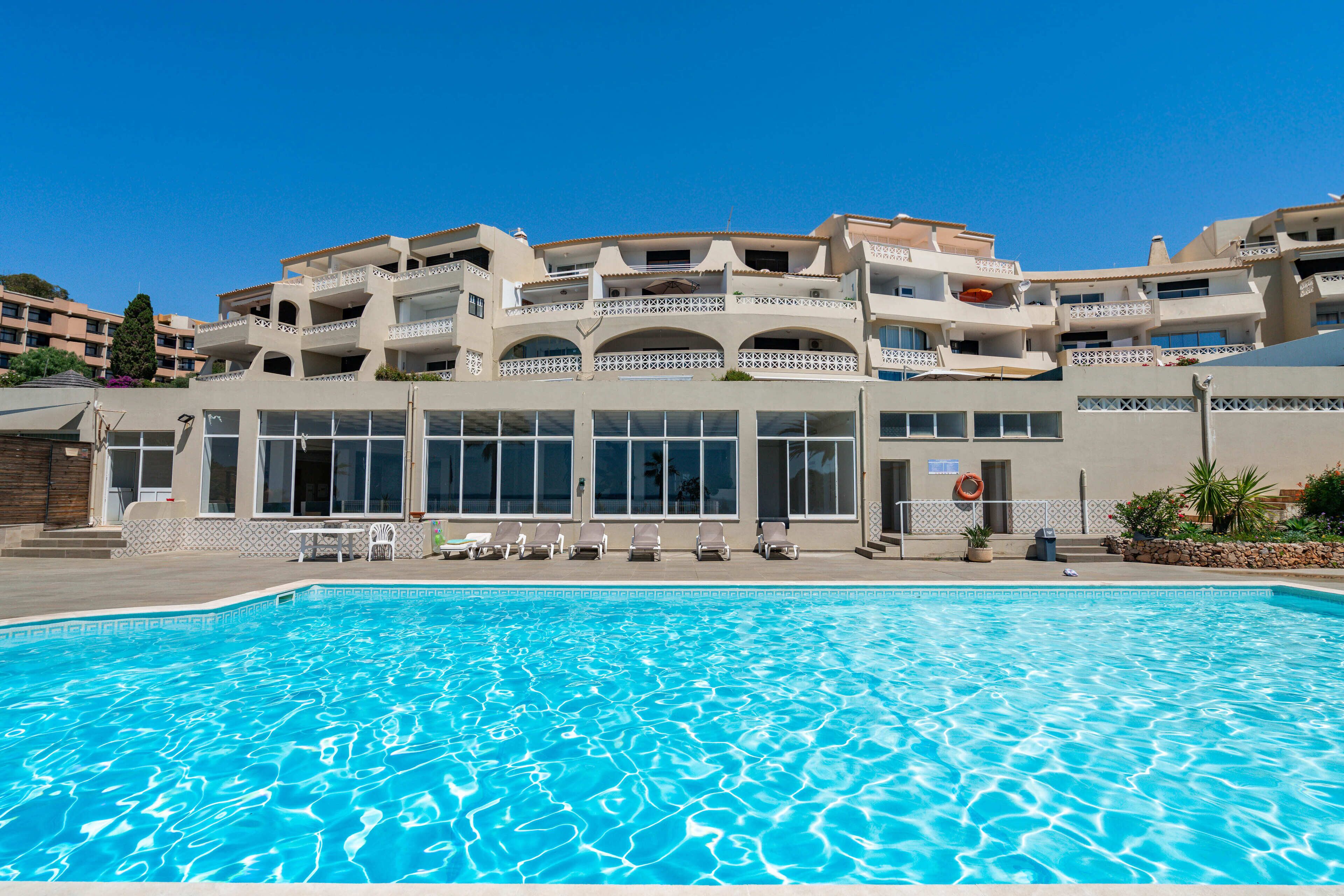 A swimming pool with lounge chairs and a building with multiple balconies and windows.