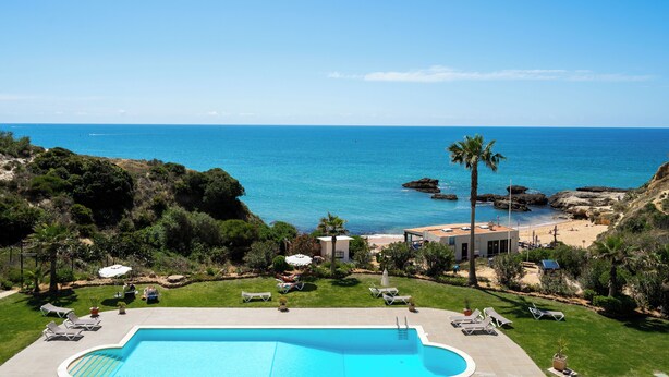 A pool area with lounge chairs and umbrellas, a view of the sea, and a rocky coastline. - Oceanfront adorable one bedroom apart in Albufeira (Albufeira)