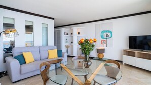 A modern living room with a glass dining table, a sofa with cushions, a TV, and a vase with flowers. - Oceanfront adorable one bedroom apart in Albufeira (Albufeira)