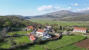 Un paysage rural avec une maison dotée d’une piscine, entourée de champs et de montagnes.