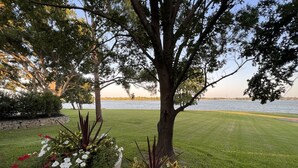 A well-maintained lawn with a stone border, large potted plants with white flowers, and a view of a body of water in the background. - Luxury Lakefront Estate - 1.6 Acres - Sleeps 12 - Boathouse + Sunset Views (Little Elm)