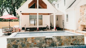 Una casa con piscina de piedra, terraza de madera y zona de patio cubierta.