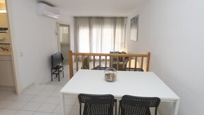 A small dining area with a white table and four black chairs, a wooden bench, and a TV on a stand.