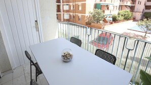 A balcony with a white table, two black chairs, and a glass vase with dried flowers.