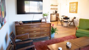 Una sala de estar con televisor de pantalla plana, muebles de madera, un sofá verde y una zona de comedor con sillas y una mesa.