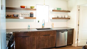 Una cocina con gabinetes de madera, lavavajillas de acero inoxidable y salpicadero de azulejos blancos.
