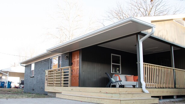 Una casa con porche cubierto, terraza de madera y un pequeño espacio de estar al aire libre.