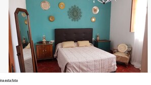 Un dormitorio con cama, mesita de noche, silla, espejo y decoración en la pared.