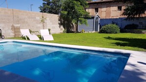 Una piscina con dos sillas de descanso y un muro de ladrillo al fondo.