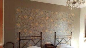 Un dormitorio con dos camas, una silla de madera, una mesita de noche y un papel tapiz floral.