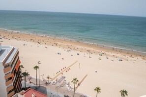 A beach with a wide sandy area, a few palm trees, and a building with balconies.