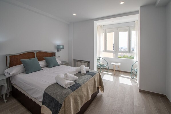 A neatly made bed with pillows and towels, a bedside table, a chair, a small table, and a window with a view.