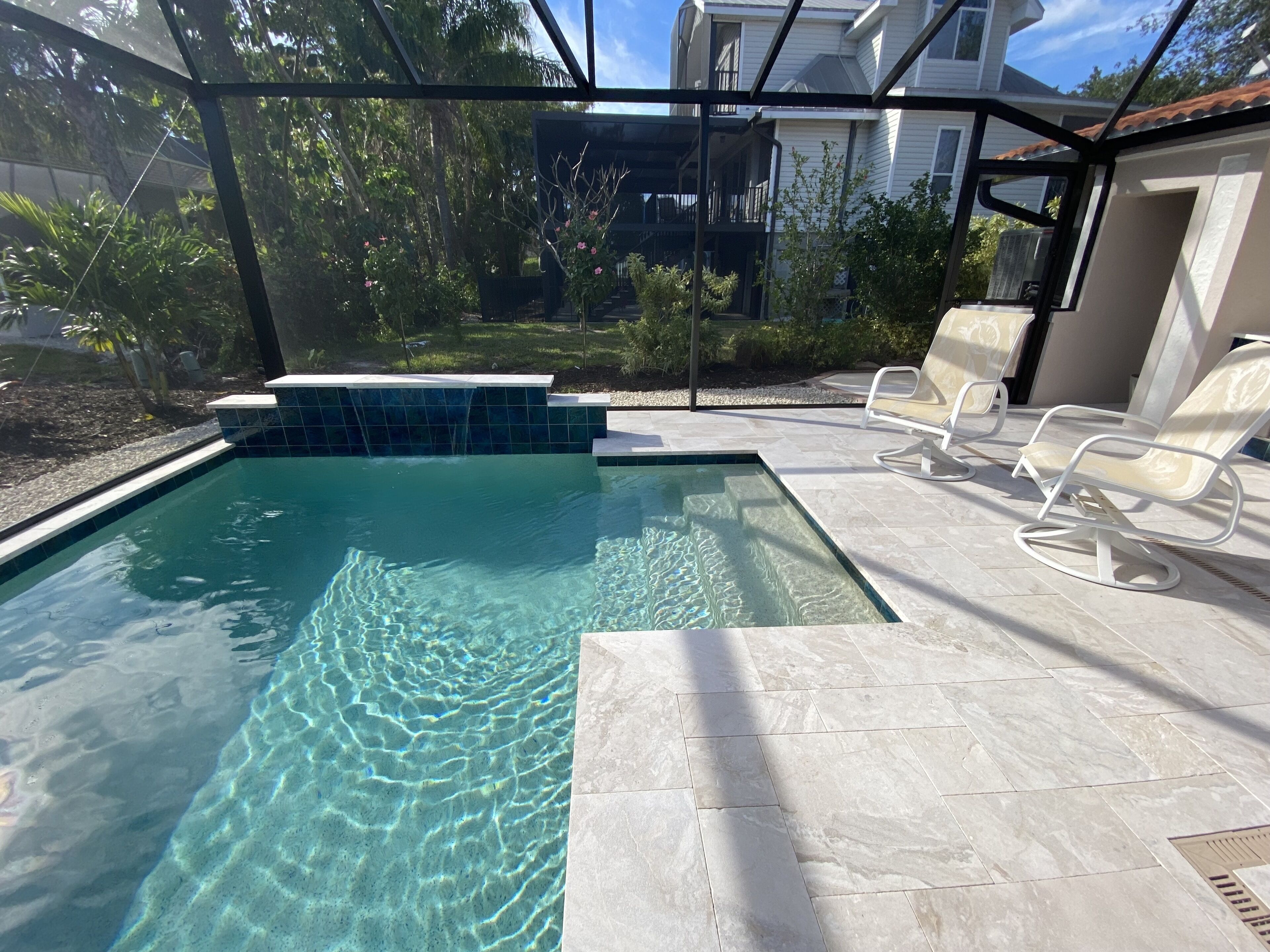A swimming pool with clear water, surrounded by a patio with lounge chairs.