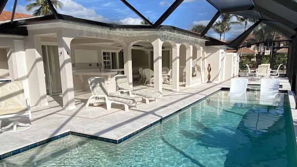 A swimming pool with clear water, surrounded by lounge chairs and a covered patio area with columns. - EASY 5-Min Walk to Beach Path! NEW Saltwater Pool & Spa, Steps to Dining & Shops (Marco Island)
