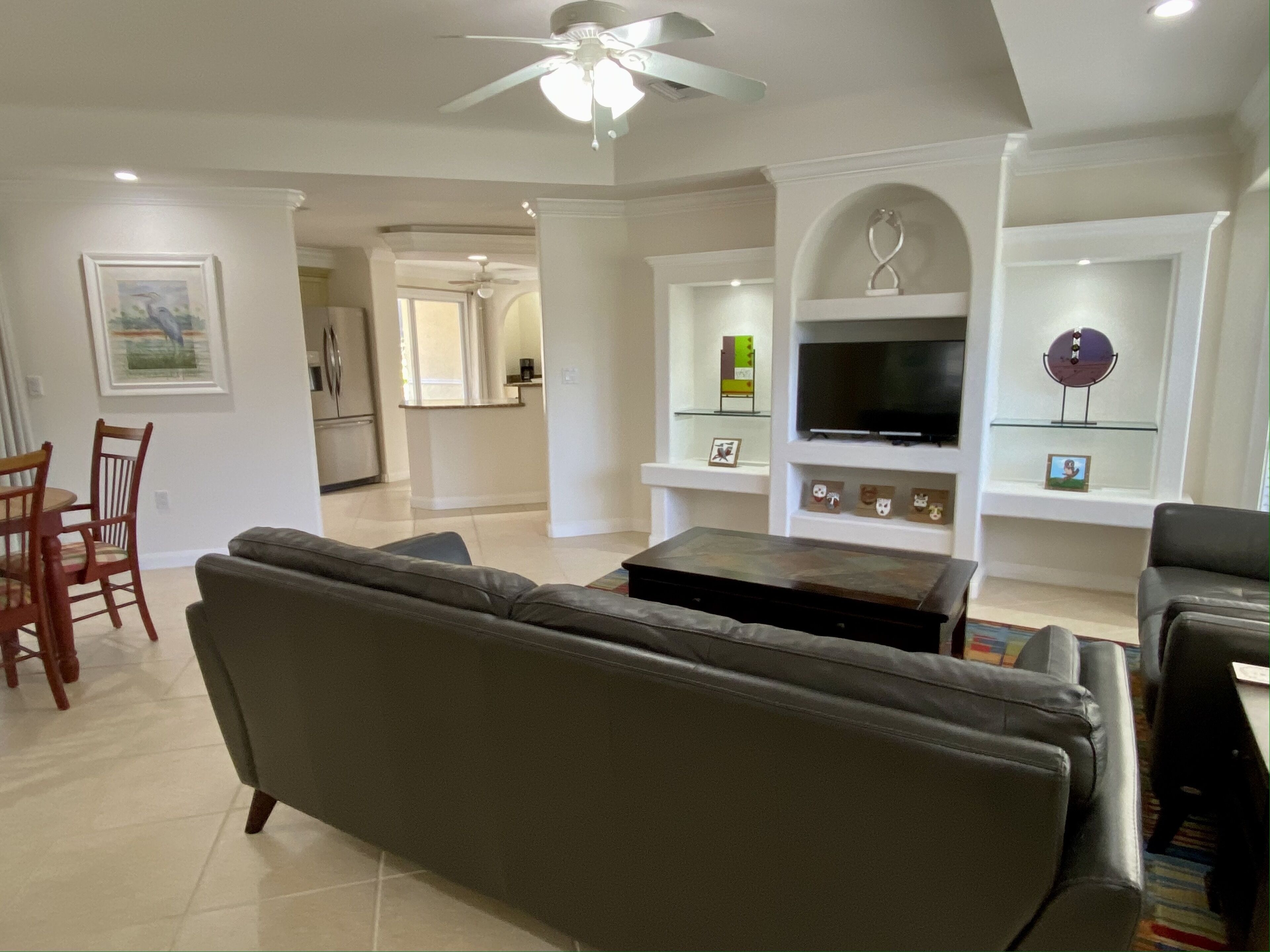 A living room with a gray sofa, a coffee table, and a TV on a white wall. There is a dining area with a wooden table and chairs.