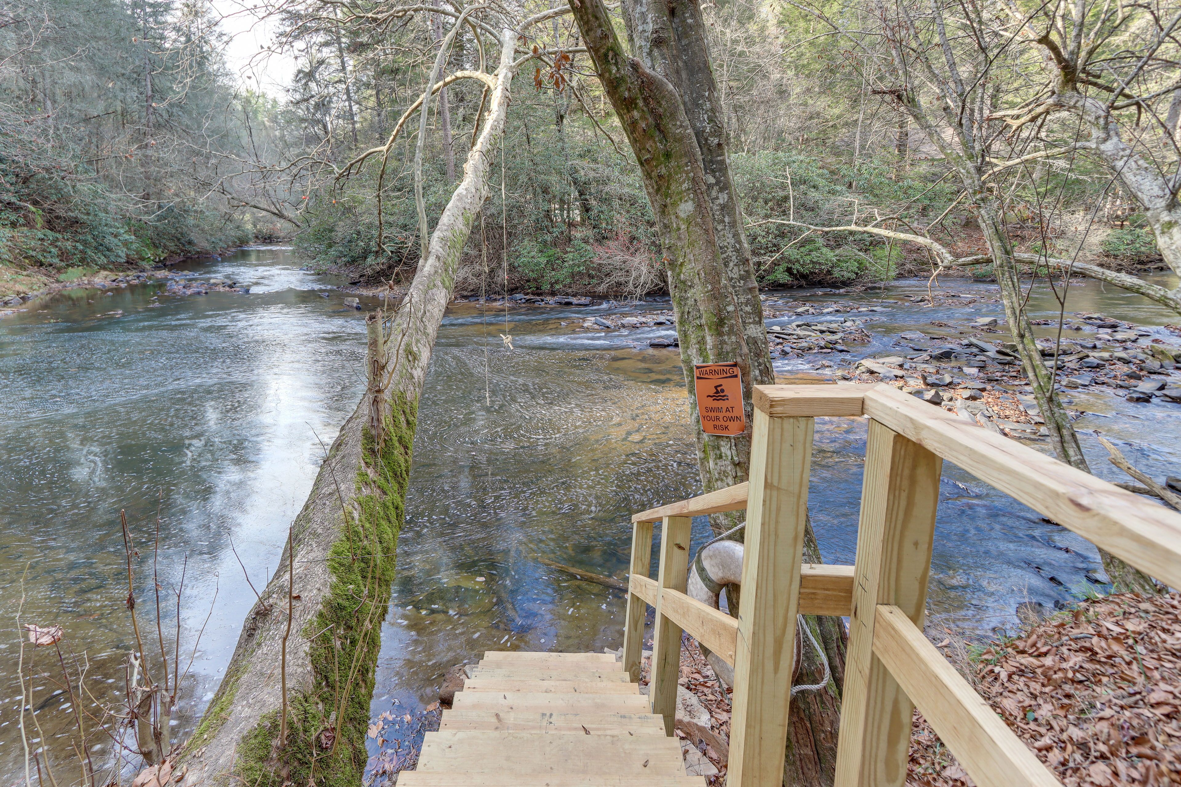 Un escalier en bois qui descend vers une rivière, avec un panneau d’avertissement.