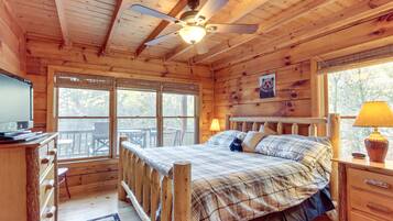 Une chambre dans une cabane en bois, avec un lit, un ventilateur de plafond, une télévision et de grandes fenêtres.