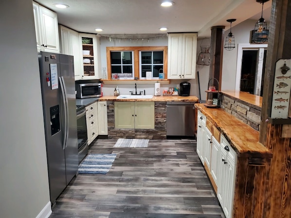 A modern kitchen with white cabinets, a stone accent wall, and a wooden countertop.