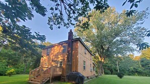 A wooden cabin with a staircase leading to a deck, surrounded by lush greenery and trees. - Fish ,Relax, Repeat.  (Conneaut)