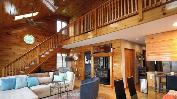 A spacious living room with a wooden staircase, a fireplace, and a dining area.