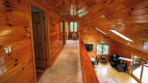 A wooden cabin interior with a loft bedroom, a dining area, and a living room.