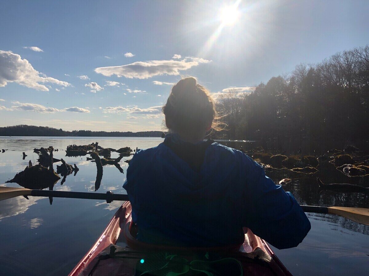 A person in a canoe on a calm body of water with a clear sky and distant land visible.