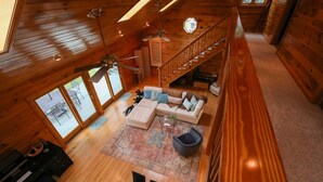 A spacious loft-style room with a wooden floor, a large sofa set, a dining table with chairs, and a staircase leading to an upper level.