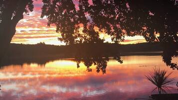Um pôr do sol sobre um lago calmo, com árvores recortadas no céu.