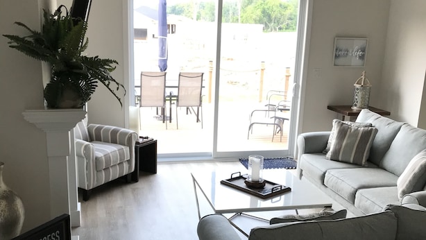 A modern living room with a grey sofa, a striped armchair, and a coffee table. There is a potted plant on a white pedestal, and a sign that reads "DOCK ACCESS".
