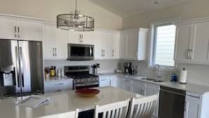 A modern kitchen with white cabinets, stainless steel appliances, a central island with chairs, and a window providing natural light.