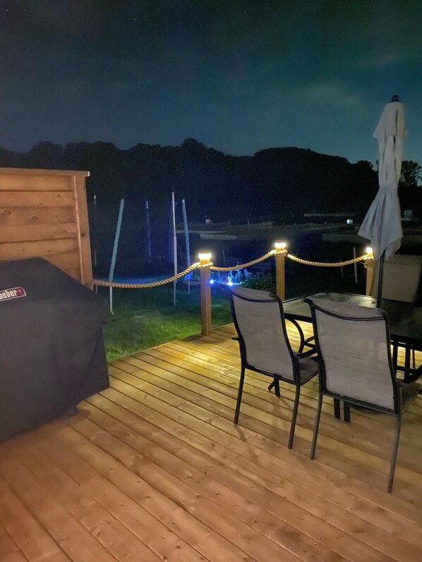 An outdoor deck with a wooden table and chairs, a covered seating area, and a rope barrier with lights. - The Dock- walk to beach & village (Port Stanley)