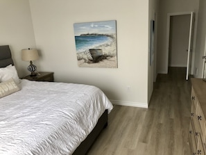 Una camera da letto con un letto, un comodino con una lampada, un quadro che raffigura una spiaggia e un settimino in legno.