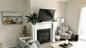 A living room with a gray sofa, a striped armchair, a flat-screen TV, a fireplace, and a plant.