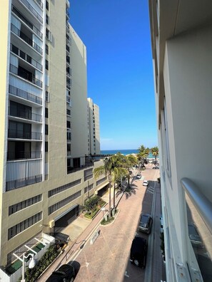 A high-rise building with multiple balconies, a parking area, and a clear view of the ocean.