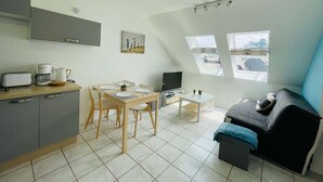 A compact living space with a kitchenette, dining area, and a sofa. - Appartement Résidence le Casino à Perros Guirec (PERROS GUIREC)