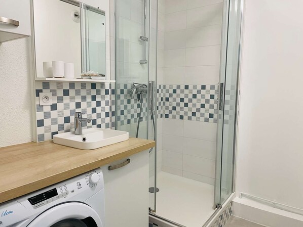 A modern bathroom with a glass-enclosed shower, a white sink with a wooden countertop, and a washing machine.