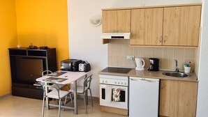 A compact kitchen with a stove, oven, and sink, a small dining table with chairs, and a yellow wall.