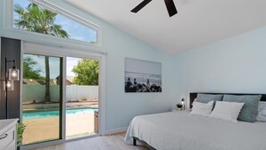 Ein Schlafzimmer mit einem großen Bett, einer Schiebetür zum Poolbereich und einem Deckenventilator.