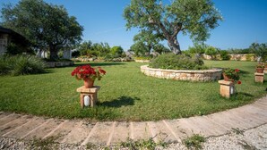 A well-maintained garden with a large tree, stone planters with flowers, and a stone wall.